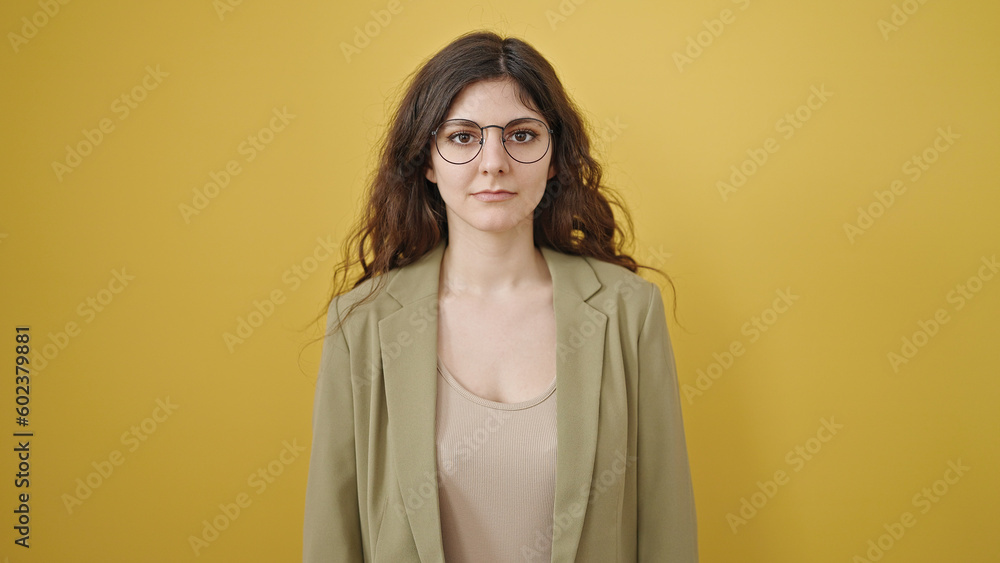 Young beautiful hispanic woman standing with serious expression over isolated yellow background Young beautiful hispanic woman standing with serious expression over isolated yellow background