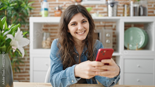 Young beautiful hispanic woman using smartphone sitting on table at dinning room