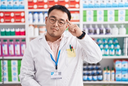 Chinese young man working at pharmacy drugstore smiling pointing to head with one finger, great idea or thought, good memory © Krakenimages.com