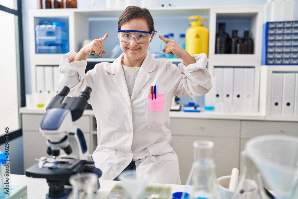 Hispanic girl with down syndrome working at scientist laboratory smiling pointing to head with both hands finger, great idea or thought, good memory Hispanic girl with down syndrome working at scientist laboratory smiling pointing to head with both hands finger, great idea or thought, good memory