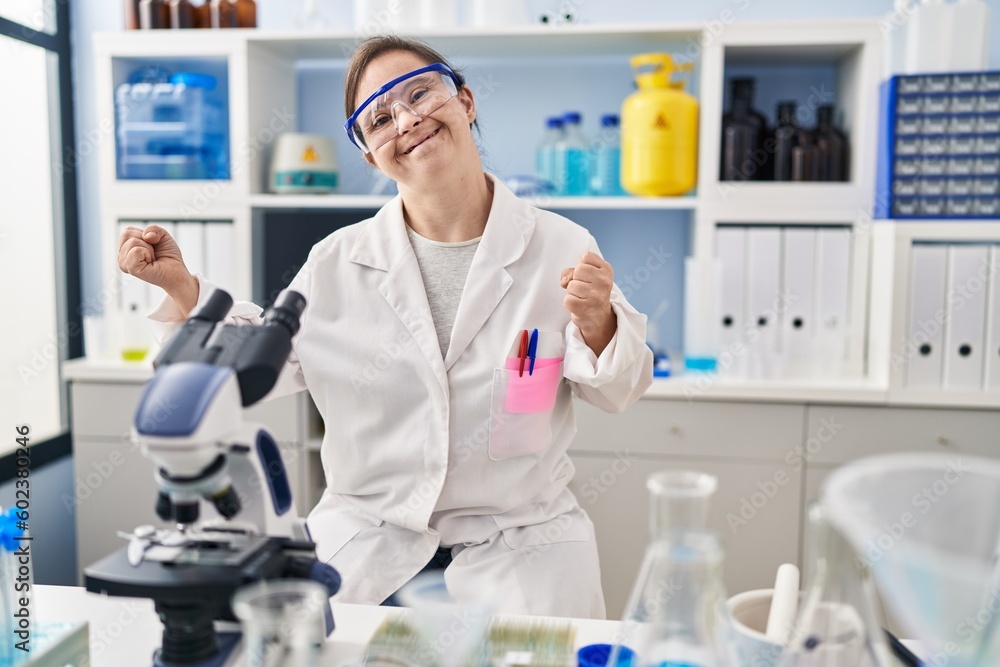 Hispanic girl with down syndrome working at scientist laboratory very happy and excited doing winner gesture with arms raised, smiling and screaming for success. celebration concept. Hispanic girl with down syndrome working at scientist laboratory very happy and excited doing winner gesture with arms raised, smiling and screaming for success. celebration concept.