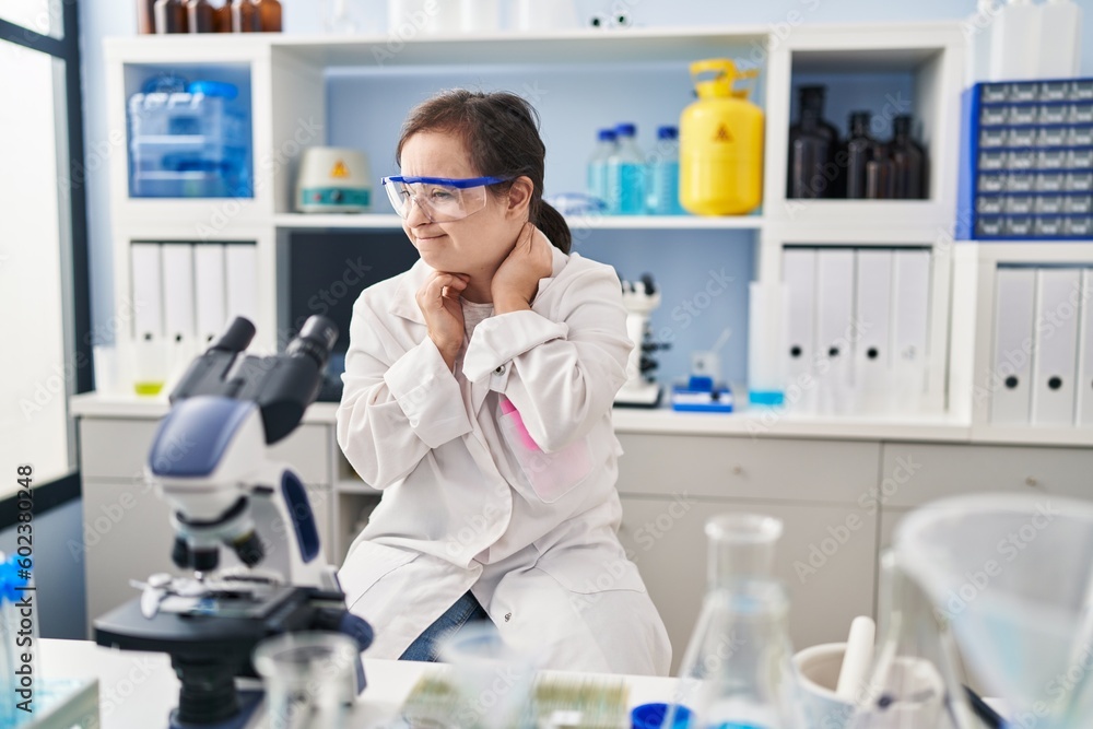 Hispanic girl with down syndrome working at scientist laboratory suffering of neck ache injury, touching neck with hand, muscular pain Hispanic girl with down syndrome working at scientist laboratory suffering of neck ache injury, touching neck with hand, muscular pain