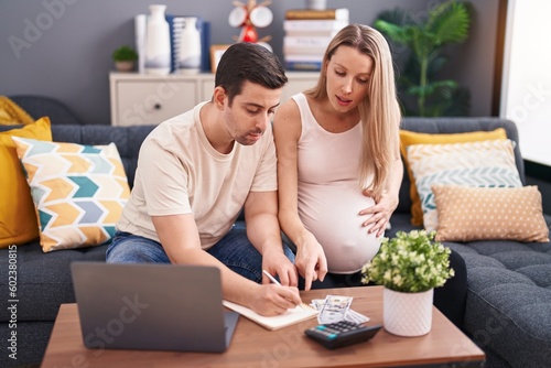 Cuadro en lienzo Man and woman couple expecting baby writing on notebook accounting at home