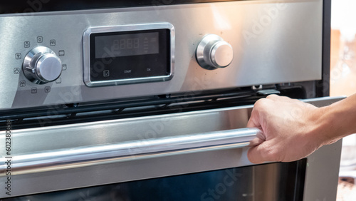 Male hand pulling oven door handle in modern kitchen. Cooking appliance for domestic kitchen.