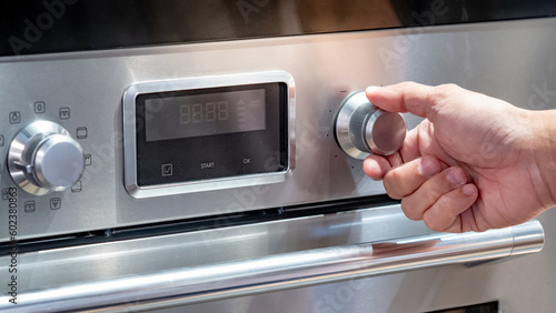 Male hand turning temperature dial knob of oven in modern kitchen. Cooking appliance for domestic kitchen.