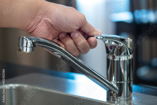 Save water or water conservation concepts. Male hand closing water tap or faucet on stainless steel sink in the kitchen.