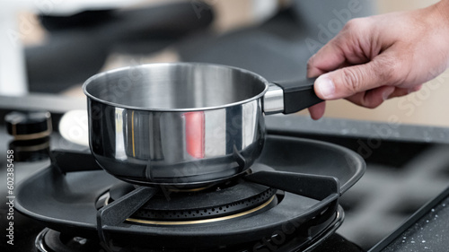 Shopping kitchen utensils concept. Male hand holding stainless steel saucepan on gas stove in kitchenware showroom store. Buying cookware for the domestic kitchen at home. © Summer Paradive