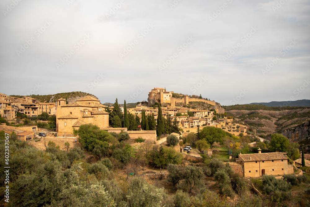 Panoramic view of the touristy medieval village of Alquezar on a hill surrounded by mountains with small brick houses and a large church at the top.