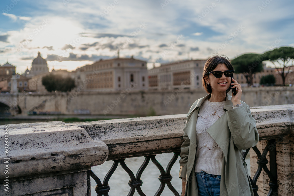 Fototapeta premium Beautiful young happy female with sunglasses talking on mobile phone in Rome Italy