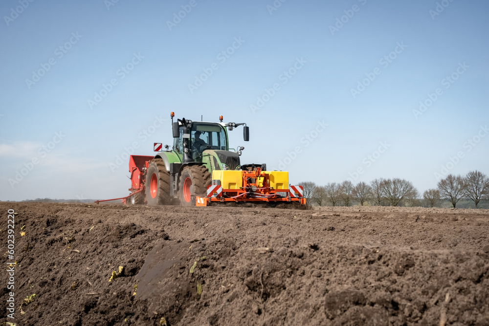 Fototapeta premium Moderne Landtechnik für die Bestellung des Katoffelackers im Einsatz - Traktor mit Kartoffellegemaschine.