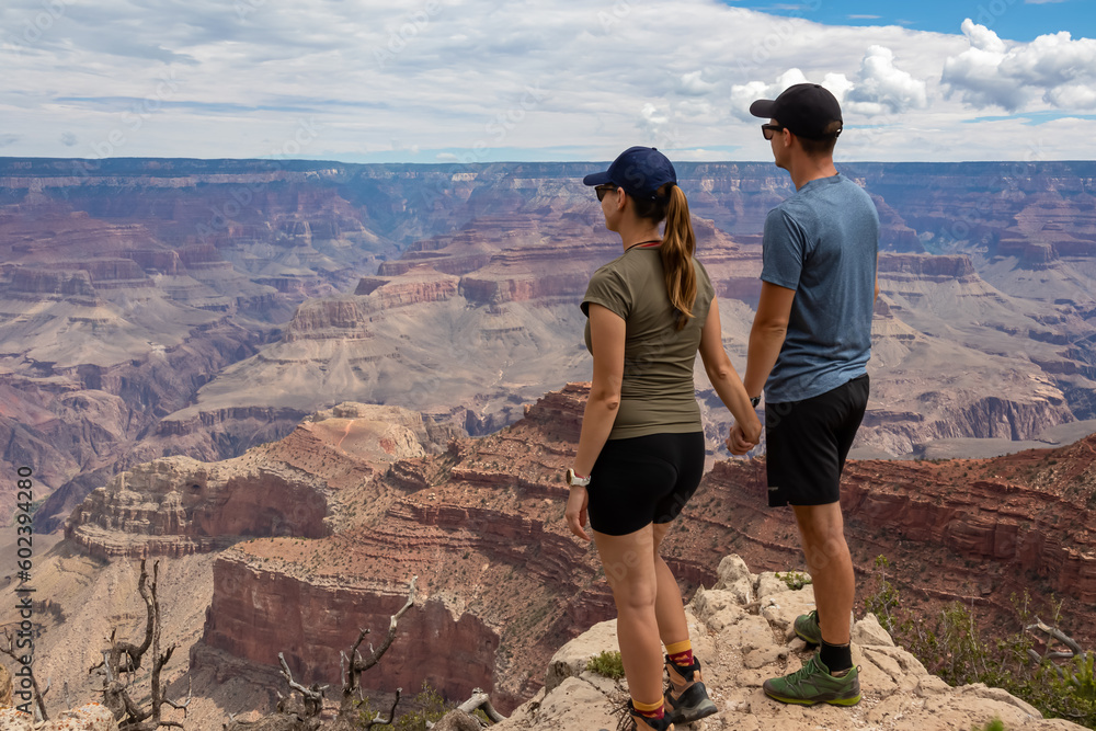 Loving couple standing on rock with scenic view from Skeleton Point on South Kaibab hiking trail at South Rim, Grand Canyon National Park, Arizona, USA. Colorado River weaving through rugged terrain