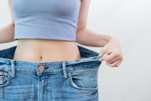 Shape slender, thin waist, attractive slim asian young woman, hand show shape her weight loss, wearing in big, large or oversize jeans, excess lose by diet and exercise. People body fit healthy.