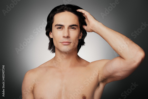 Young shirtless man holding hand in hair and looking at camera against grey background
