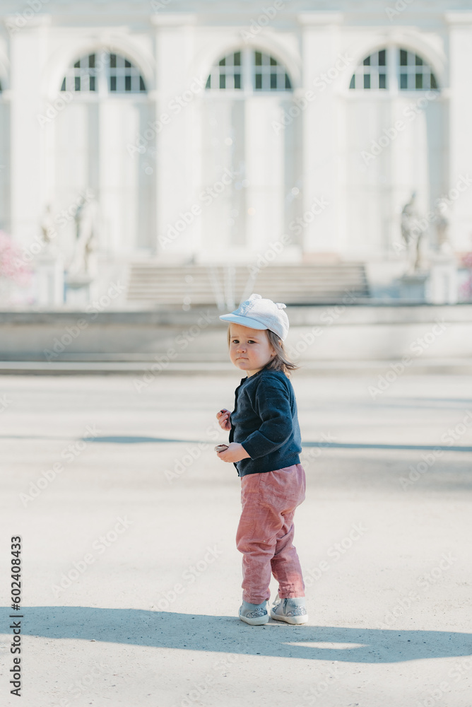 A female toddler with her back in the yard of the European palace.