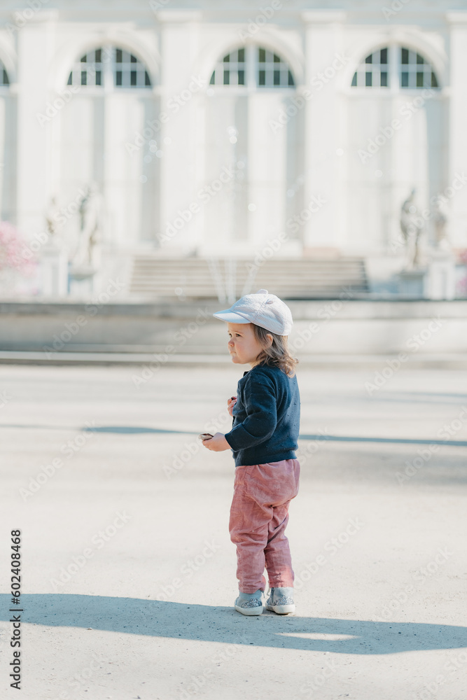 A female toddler with her back in the yard of the European palace.