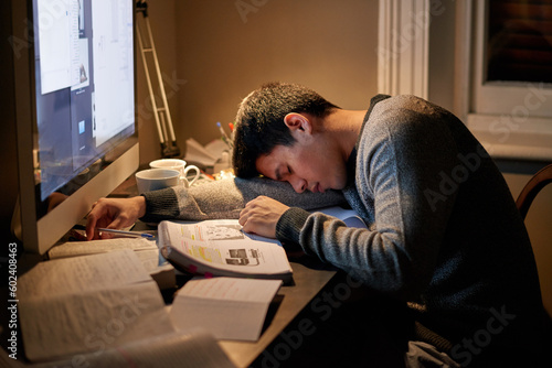 Young student, books and sleeping near screen or studying late into the night or resting on table and reading for examination. Tired, research and hard working for test paper or computer at home