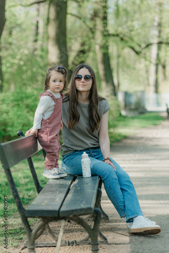 Obraz na płótnie A female toddler in velvet overall is on the bench with her mother. w salonie