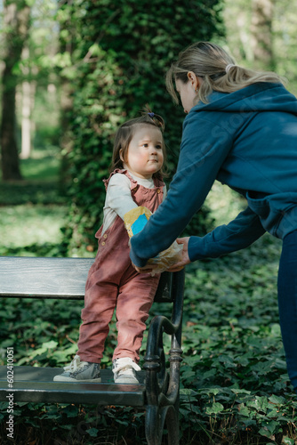 Obraz na płótnie A female toddler in velvet overall is on the bench with her mother. w salonie