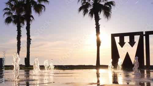 Tourist place, embankment of resort town of Batumi in Georgia, beat fountains against background of sea and sunset. Nearby grow decarative plants, palm trees, street cafes. People are coming. photo