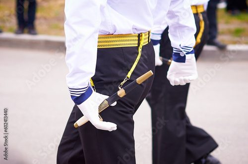 A naval officer with a dagger on his belt in dress uniform marches at a military parade.