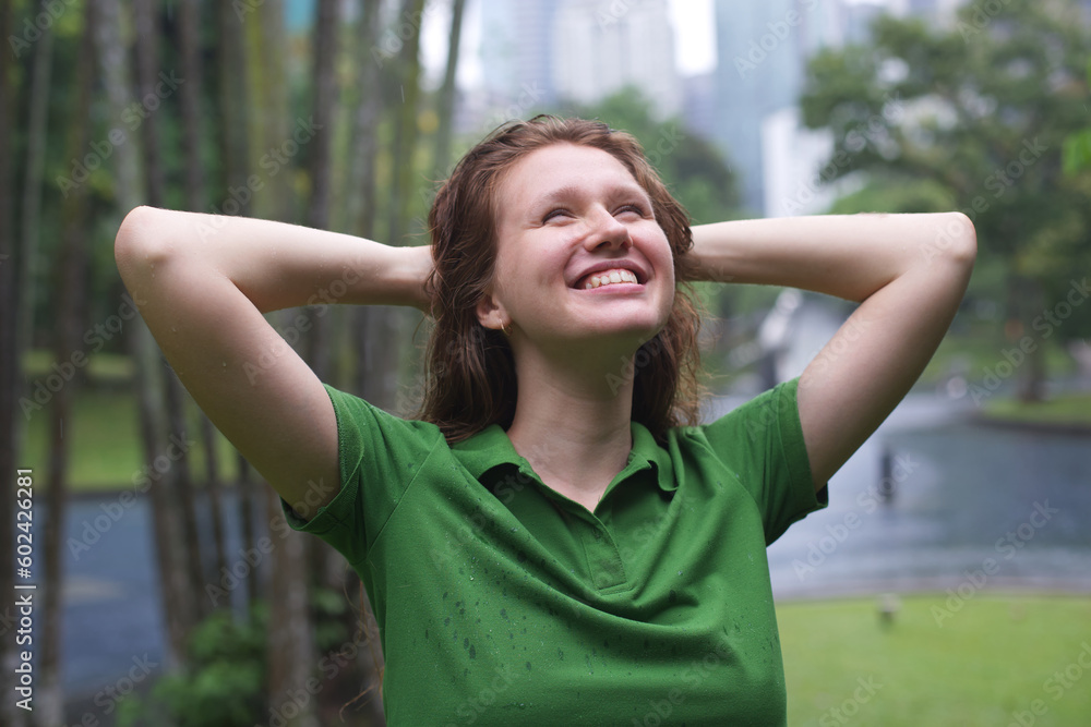 Positive young woman smiling during the rain in the park. Cheerful female enjoying the rain outdoors. Woman looking up and catching the rain drop with hands. Breath deep and relax Positive young woman smiling during the rain in the park. Cheerful female enjoying the rain outdoors. Woman looking up and catching the rain drop with hands. Breath deep and relax