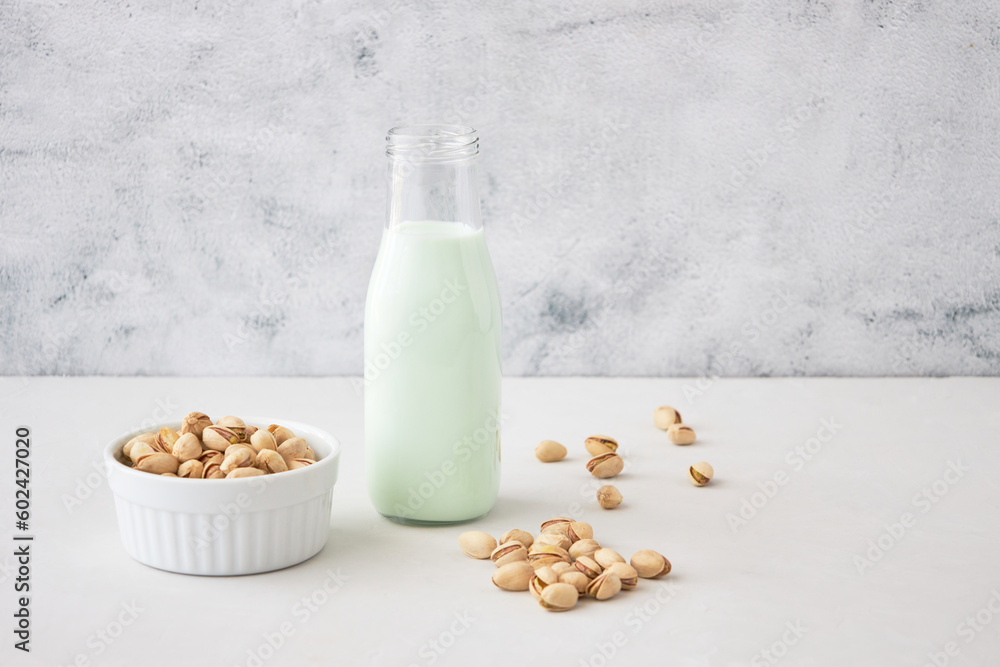 Pistachio milk in a bottle on a gray table next to pistachios. Vegetable milk. Nut milk for vegans Pistachio milk in a bottle on a gray table next to pistachios. Vegetable milk. Nut milk for vegans