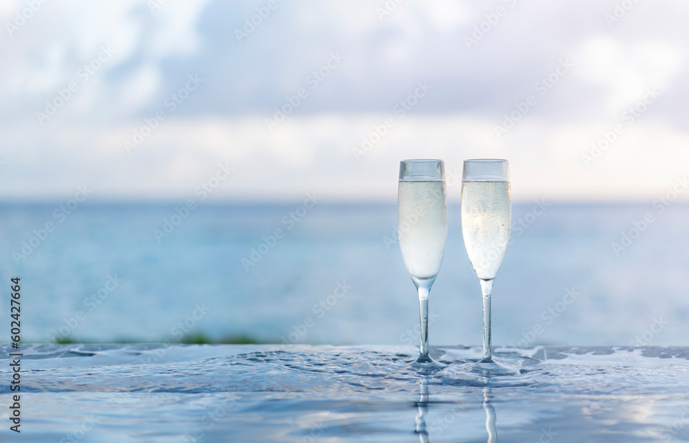 Two glasses of champagne on the side of the infinity pool against the backdrop of a sunset in the Maldives