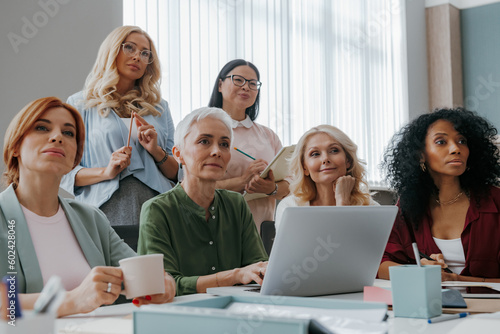Group of mature women listening to speaker while having business training in office