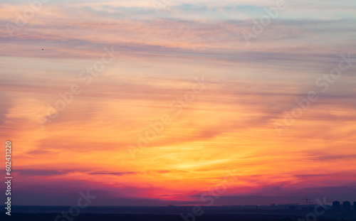 Fototapeta Naklejka Na Ścianę i Meble -  Beautiful sunset with multi -colored clouds. The silhouettes of houses and cranes on the horizon. Soft focus