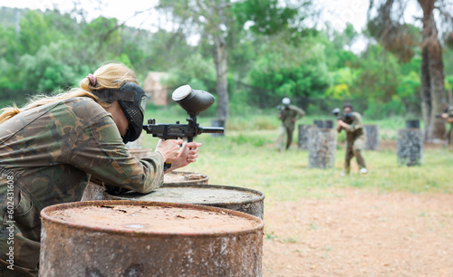Woman paintball player in mask aiming with gun at opposing team outdoors