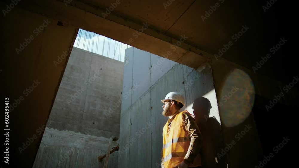 Business building concept. lifestyle worker in a helmet silhouette idea concept. an engineer in a hard hat stands at the wall in the house inside the construction site. Slow motion Business building concept. lifestyle worker in a helmet silhouette idea concept. an engineer in a hard hat stands at the wall in the house inside the construction site. Slow motion