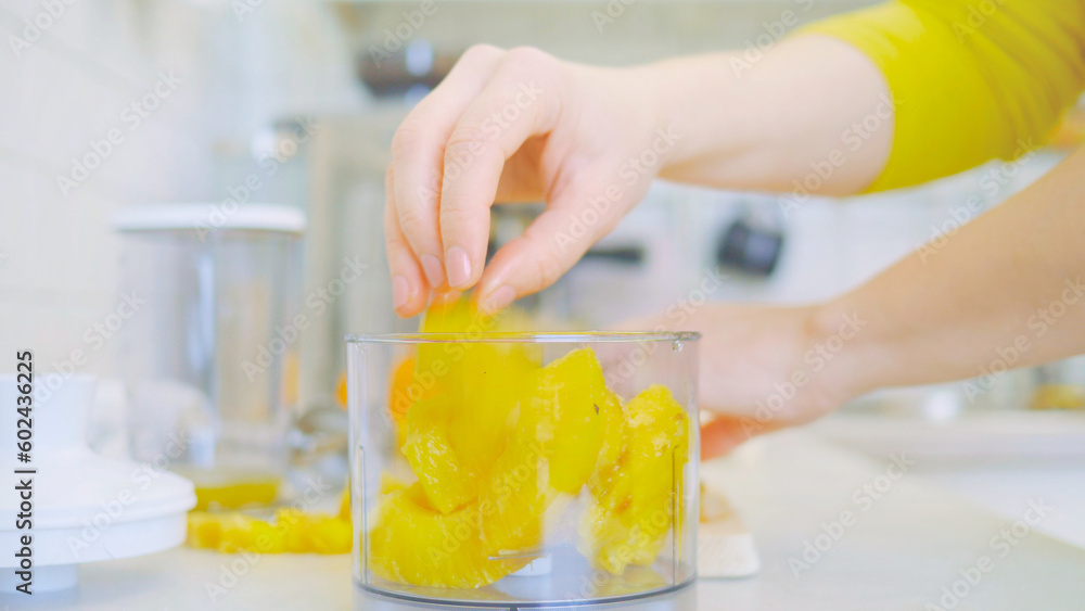 In a kitchen, a young woman prepares a healthy smoothie using a blender. Surrounding her are fresh fruits, including sliced pineapple on a wooden cutting board. nutrition and healthy eating.