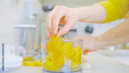 Obraz na płótnie In a kitchen, a young woman prepares a healthy smoothie using a blender. Surrounding her are fresh fruits, including sliced pineapple on a wooden cutting board. nutrition and healthy eating. w salonie