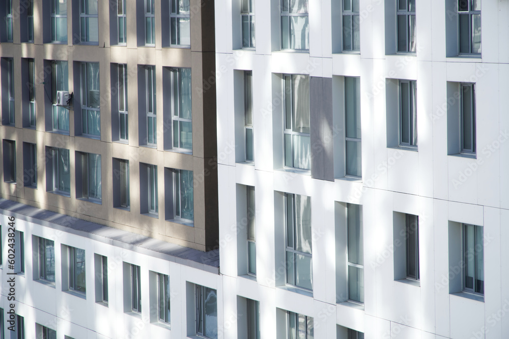 Facade of a modern two-tone multi-storey residential building in the morning sun. Windows and walls. Construction background Facade of a modern two-tone multi-storey residential building in the morning sun. Windows and walls. Construction background