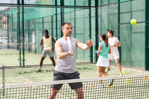 Man training to play tennis on the padel court outdoor. Athletes training in the background © JackF