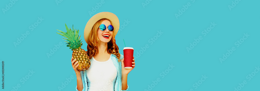 Summer portrait of happy smiling woman looking away with cup of juice and pineapple wearing straw hat, sunglasses on blue background