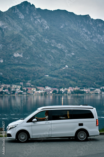 Older man driving rv camper van on vacation trip. Smiling mature active traveler sitting in campervan trailer enjoying camping tourism in nature park with lake and mountains travel journey. Vertical