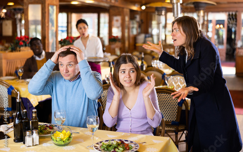 Woman catching her husband with young mistress in restaurant. Cheating in marriage concept..