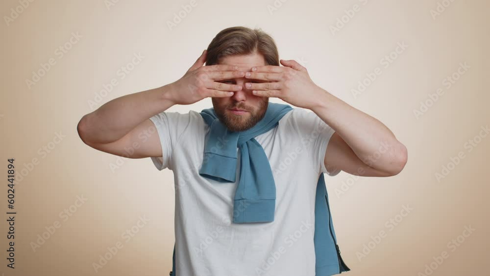 Nosy curious caucasian man closing eyes with hand and spying through fingers, hiding and peeping, binocular gesture, exploring way, seeking something in distance. Young guy on beige studio background Nosy curious caucasian man closing eyes with hand and spying through fingers, hiding and peeping, binocular gesture, exploring way, seeking something in distance. Young guy on beige studio background
