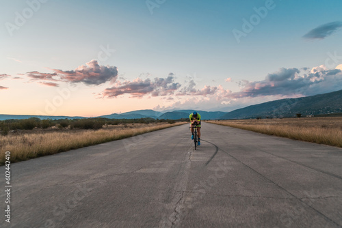  Triathlete riding his bicycle during sunset, preparing for a marathon. The warm colors of the sky provide a beautiful backdrop for his determined and focused effort. © .shock