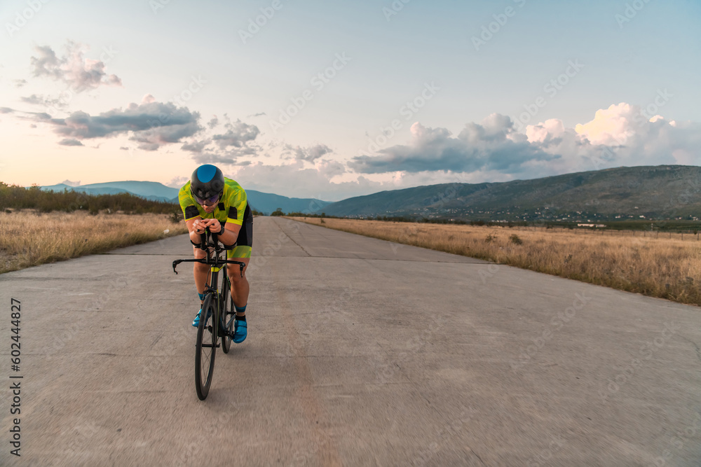 Fototapeta premium Triathlete riding his bicycle during sunset, preparing for a marathon. The warm colors of the sky provide a beautiful backdrop for his determined and focused effort.