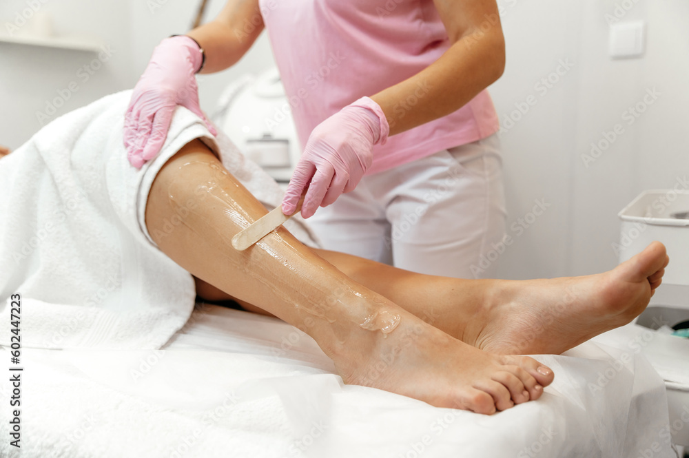 Fototapeta premium Application of the gel on the leg before the procedure. Hair removal cosmetology procedure. Laser epilation and cosmetology. Cosmetologist prepares leg before laser hair removal, applies gel on leg