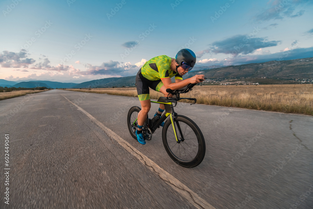 Fototapeta premium Triathlete riding his bicycle during sunset, preparing for a marathon. The warm colors of the sky provide a beautiful backdrop for his determined and focused effort.