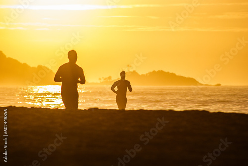 silhouette of people running at dawn on leblon beach in rio de janeiro.