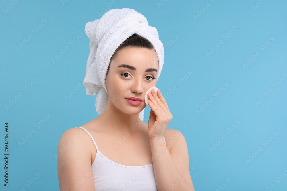 Beautiful woman in terry towel removing makeup with cotton pad on light blue background, space for text Beautiful woman in terry towel removing makeup with cotton pad on light blue background, space for text