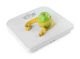 Weight loss concept. Ripe apple and measuring tape on scales isolated on white