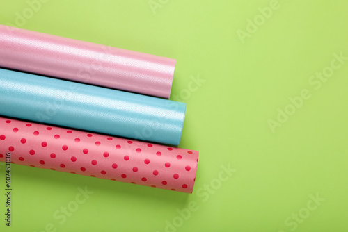 Rolls of colorful wrapping papers on green background, flat lay. Space for text