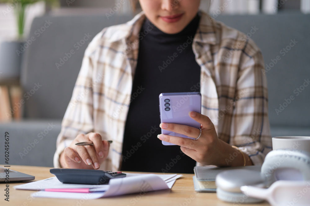Young woman paying bills online on smartphone and calculating household finances or taxes on machine. Young woman paying bills online on smartphone and calculating household finances or taxes on machine.