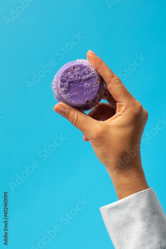 A piece of handmade soap in a woman's hand on a blue background. Natural soap, cosmetics.