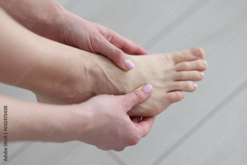 Woman massages painful foot joints with hands in light room